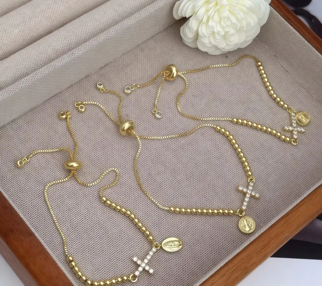 Pulsera ajustable dorada con dije de cruz con circones y medalla religiosa/ Adjustable Gold Bracelet with Cross Charm, Cubic Zirconia, and Religious Medal.